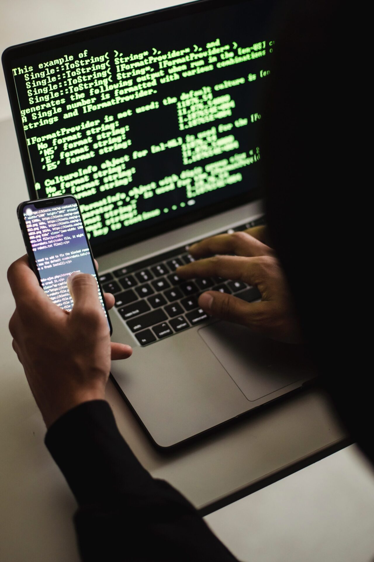 Mobile-Malware-Has-Increased-500-What-Should-You-Do-scaled.jpg Free Unrecognizable hacker with smartphone typing on laptop at desk Stock Photo