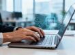 Hands typing on a laptop keyboard with digital patterns.